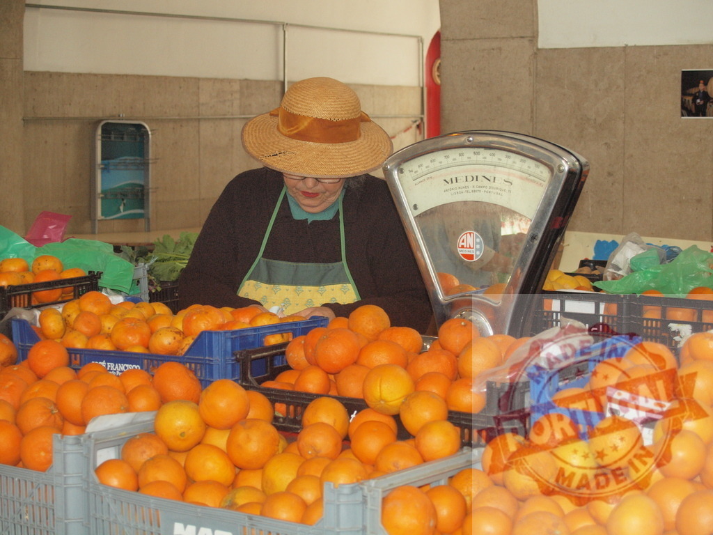 Seller wearing hat weighing oranges at market stall | Woman wearing a straw hat and apron weighing fresh oranges at a market stall - Realized with Pictrs.com