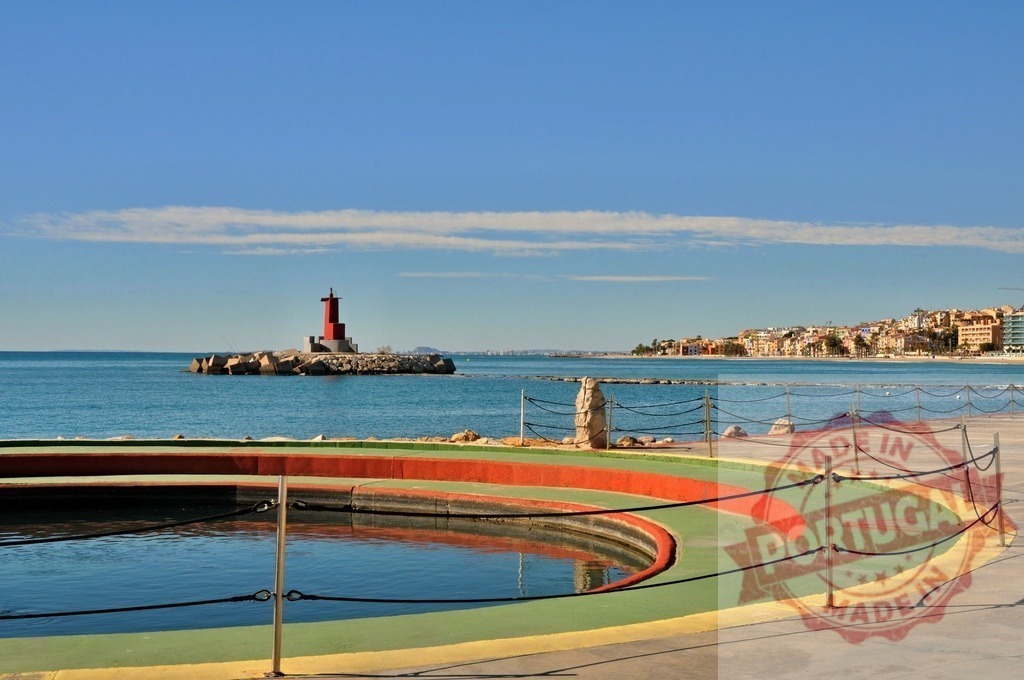Villajoyosa lighthouse, sea, coastal town, and harbor pool | Red lighthouse standing on rocky breakwater with town along the coast and colorful harbor pool - Realized with Pictrs.com