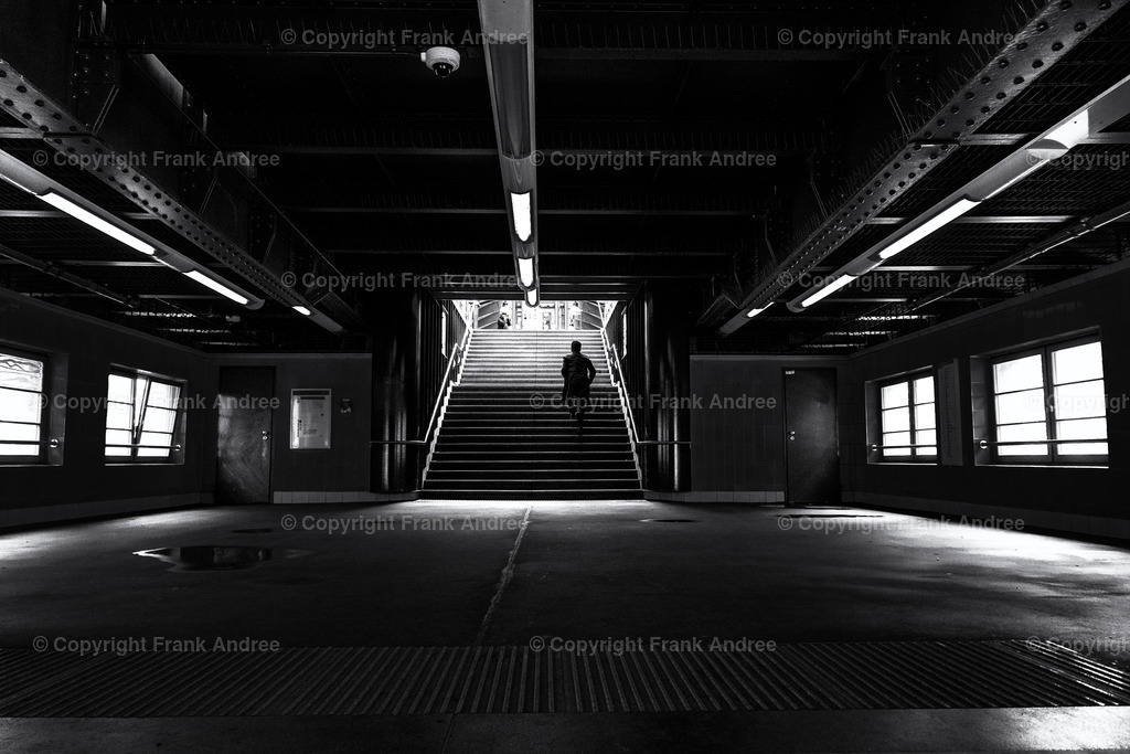 U Bahnhof Berlin Schönhauser Allee | Ein Mann geht eilig die Treppe zum Bahnsteig auf dem U Bahnhof Berlin Schönhauser Allee hinauf. Straßenfotografie aus Berlin in schwarz und weiß. - Realisiert mit Pictrs.com