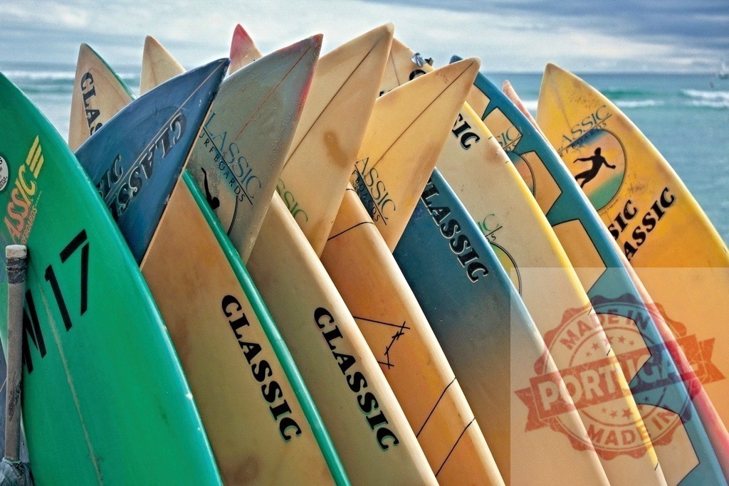 Colorful surfboards standing on the beach waiting for surfers | Many classic surfboards standing upright on a rack near the ocean, ready for riding the waves - Realisiert mit Pictrs.com