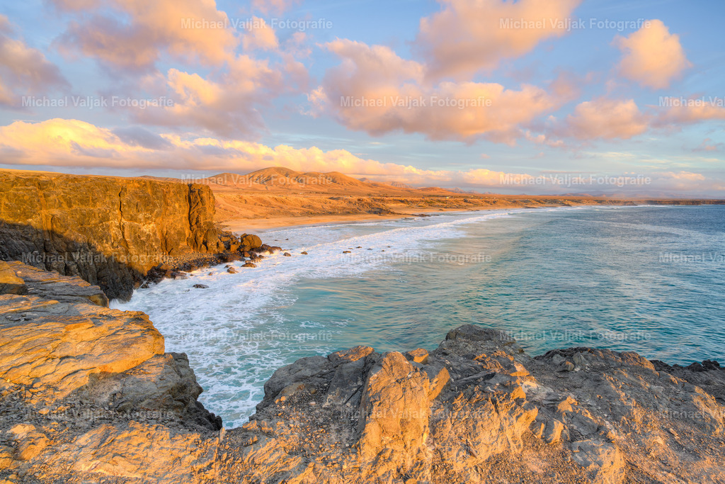 Küste bei El Cotillo auf Fuerteventura | An der Küste von El Cotillo steht die Sonne schon tief und taucht Felsen, Wasser und Himmel in ein warmes Orange. Die Wellen brechen ruhig gegen die dunklen Lavaklippen, während das Licht die Kanten weich zeichnet. Die Farben wirken intensiver, die Schatten länger, und die ganze Szene bekommt diese stille, fast zeitlose Stimmung, die nur der späte Nachmittag auf Fuerteventura erzeugt. - Realisiert mit Pictrs.com