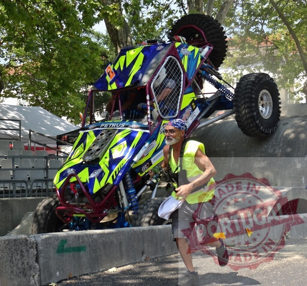 Buggy climbing a concrete pipe during an off-road competition with race marshal running | Race marshal running near a buggy climbing a concrete pipe during an off-road competition - Realized with Pictrs.com