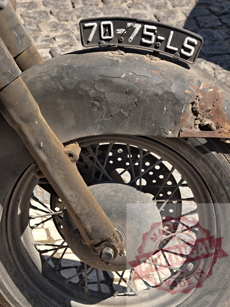 Vintage motorcycle front wheel and rusty fender | Vintage motorcycle front wheel with an aged, rusty fender and weathered license plate - Realized with Pictrs.com