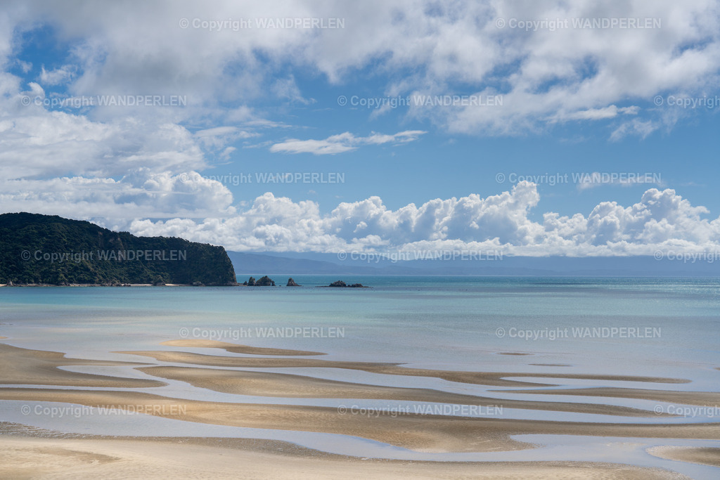 Wainui Bay | Ein einsamer Strand an der Wanui Bay, ist unter einem teilweise bewölkten Himmel abgebildet. Der Vordergrund zeigt einen weiten Sandstrand vielen kleinen Sandbänken. Hinter dem Strand erstreckt sich das ruhige, türkisfarbene Wasser der Bucht bis zu einem felsigen, bewaldeten Vorsprung links. Im Hintergrund ragen mehrere Felsformationen aus dem Wasser, und verschwommene Berge bilden den Horizont. Die Szene zeigt die natürliche Schönheit und die friedliche Atmosphäre dieses abgelegenen Ortes. - Realisiert mit Pictrs.com