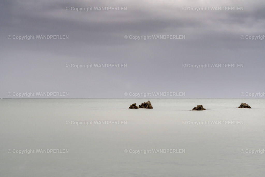 Kaikoura – Herbstliche Stille / Kaikoura – Autumnal tranquility | Herbst in Kaikoura, Neuseeland – eine friedliche Meereslandschaft, in der nur wenige Felsen die ruhige Wasseroberfläche durchbrechen. Das sanfte Licht und der bedeckte Himmel schaffen eine meditative Atmosphäre und unterstreichen die stille Schönheit der Natur. - Realisiert mit Pictrs.com