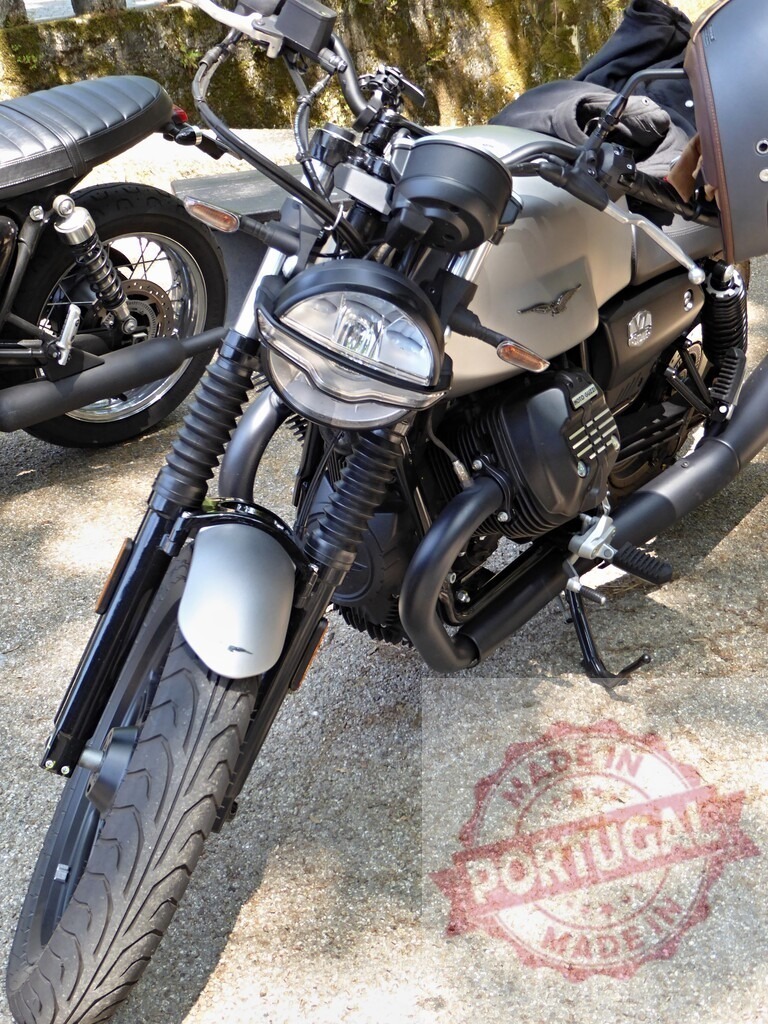 Moto Guzzi V7 Stone motorcycle parked on gravel road | Front view of a silver Moto Guzzi V7 Stone motorcycle parked on a gravel road, showcasing its design and features - Realized with Pictrs.com