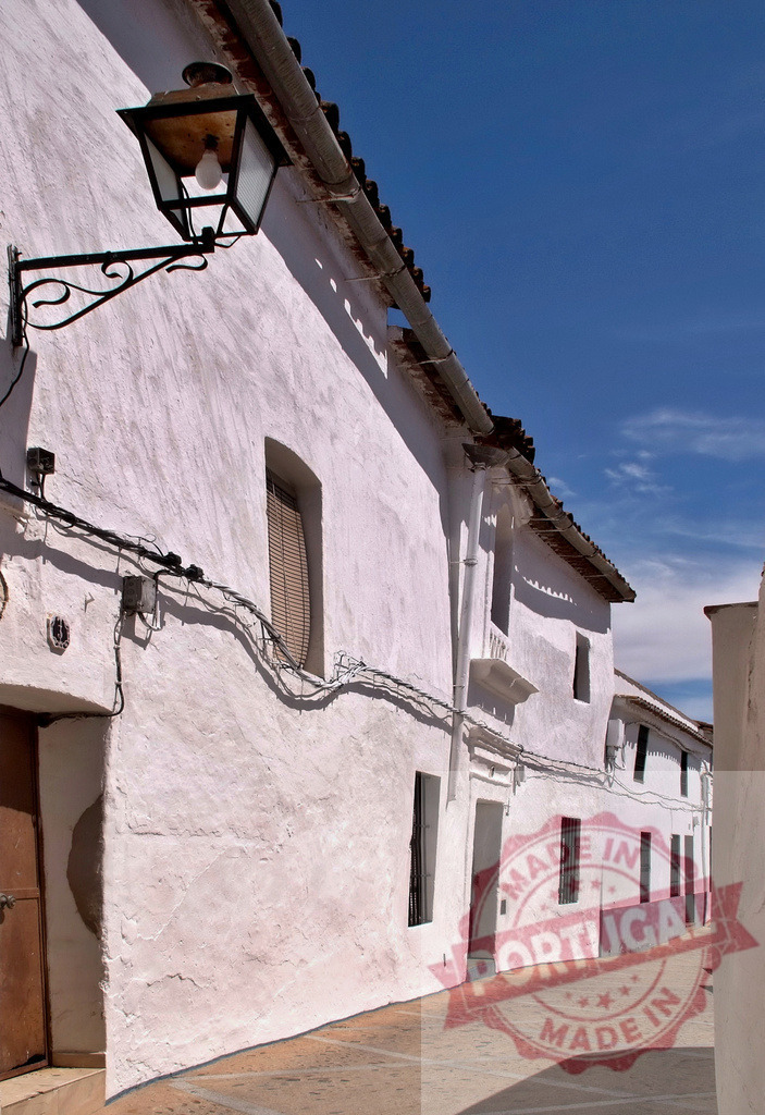 Traditional white buildings lining Spanish street with lantern. Extremdura - Spain | White houses creating a quaint street scene with a decorative lantern under blue sky - Realized with Pictrs.com