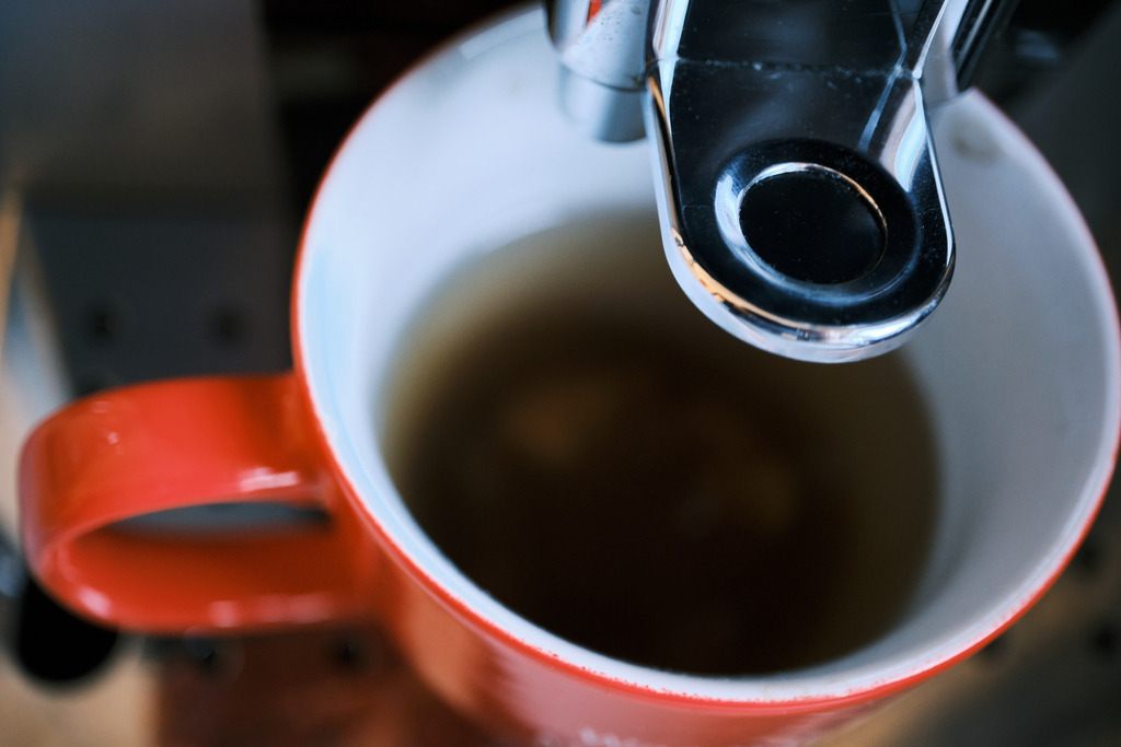 roter Becher unter einer Kaffeemaschine mit Durchlaufwasser | Wien, Austria - February 28, 2023: roter Becher unter einer Kaffeemaschine mit Durchlaufwasser. - Realisiert mit Pictrs.com