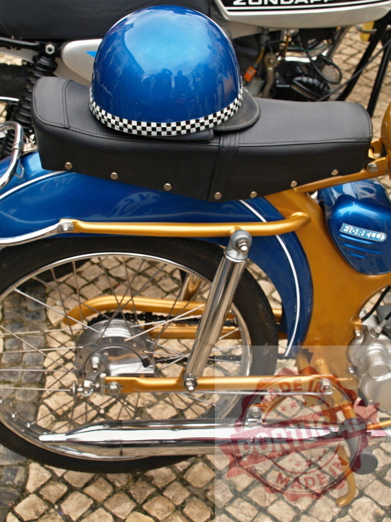 Blue helmet resting on a vintage moped seat | Shiny blue helmet with checkered stripe resting on the black seat of a parked golden and blue vintage moped - Realisiert mit Pictrs.com