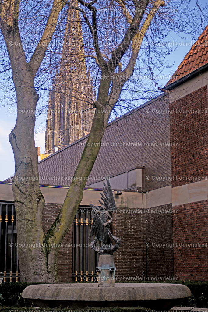 St.-Michaels-Brunnen mit Himmelsleiter der Lambertikirche Münster | Der St.-Michaels-Brunnen zeigt den Heiligen Michael auf einem Drachen. Im Hintergrund ist die Himmelsleiter der Lambertikirche zu sehen. - Realisiert mit Pictrs.com