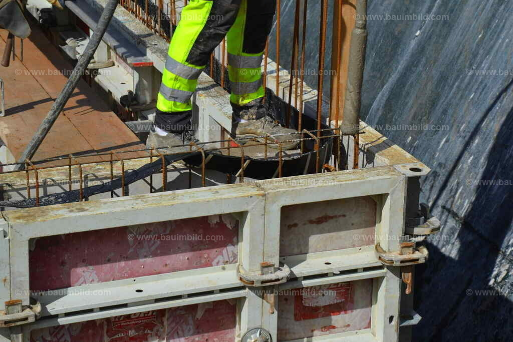Betoneinbau Wände  | Arbeiter mit Betonrüttelflasche stehend auf Wandschalung aus Aluschalung für bewehrte Betonwand