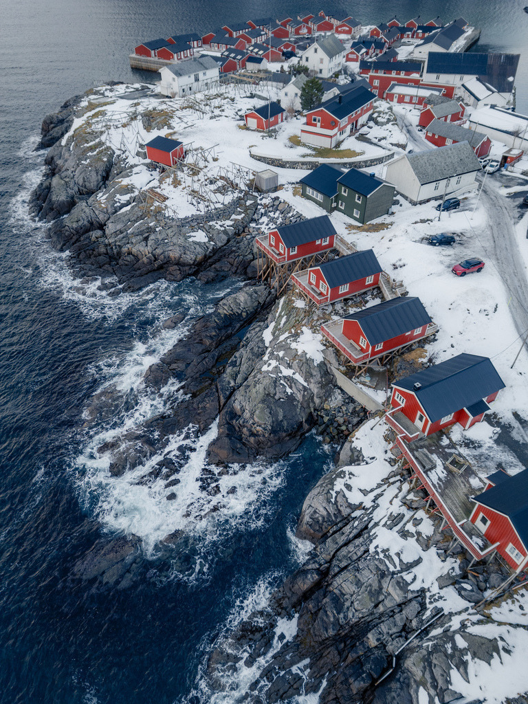 Norwegischer Küstenort aus der Vogelperspektive | Rote Häuser und verschneite Wege ziehen sich entlang einer felsigen norwegischen Küste. Die senkrechte Luftaufnahme betont die grafische Struktur des Ortes zwischen Meer, Felsen und Schnee. - Realisiert mit Pictrs.com