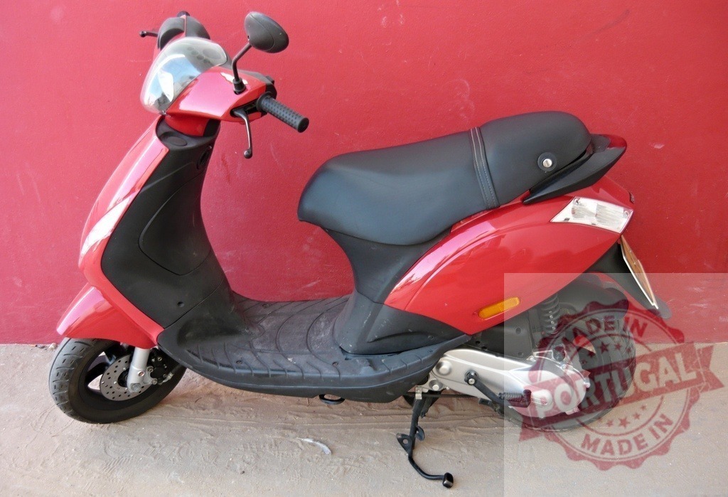 Red scooter parked near a red wall representing urban mobility | Shiny red scooter parked near a red wall, representing freedom and urban mobility - Realized with Pictrs.com