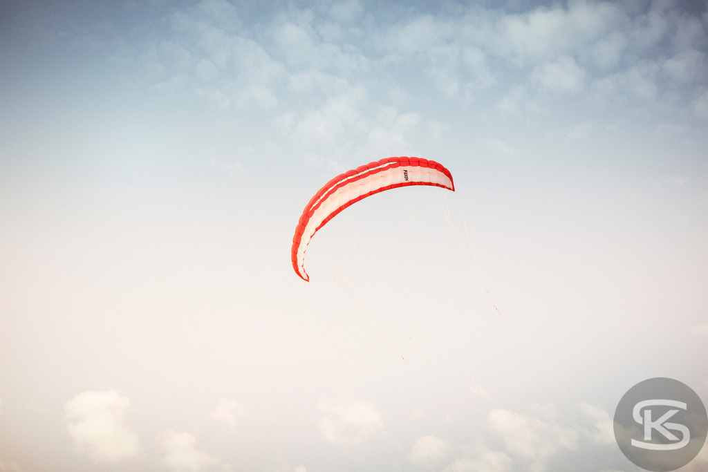 Roter und weißer Kite am Himmel | Ein dynamisches Bild eines rot-weißen Kites, der hoch am bewölkten Himmel schwebt. Die Aufnahme fängt die Leichtigkeit und Bewegung des Kitesurfens oder Kitefliegens ein und erzeugt eine atmosphärische Stimmung über den Wolken. - Realisiert mit Pictrs.com