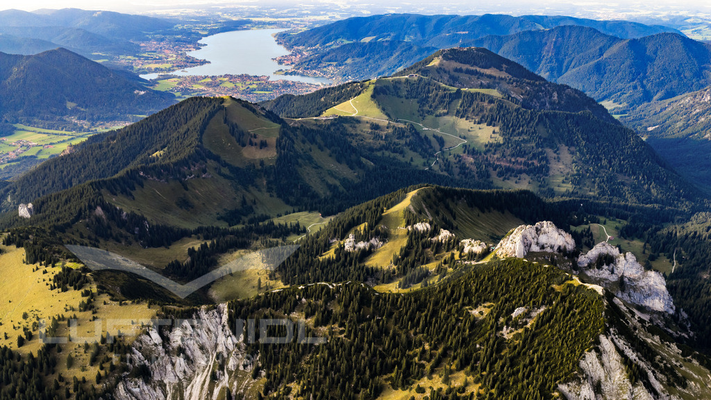 Panorama über die Berge auf das Tegernseer Tal; S44 | Die eindrucksvolle Voralpenlandschaft rund um den Tegernsee. Im Vordergrund ragen die markanten Felsformationen des Blankenstein und die grünen Berggrate von Wallberg und Setzberg hervor, dahinter breitet sich der Tegernsee mit seinen Uferorten aus. Der Blick verbindet alpine Höhen mit dem Tal und vermittelt die Nähe von Bergen und See. - Realisiert mit Pictrs.com