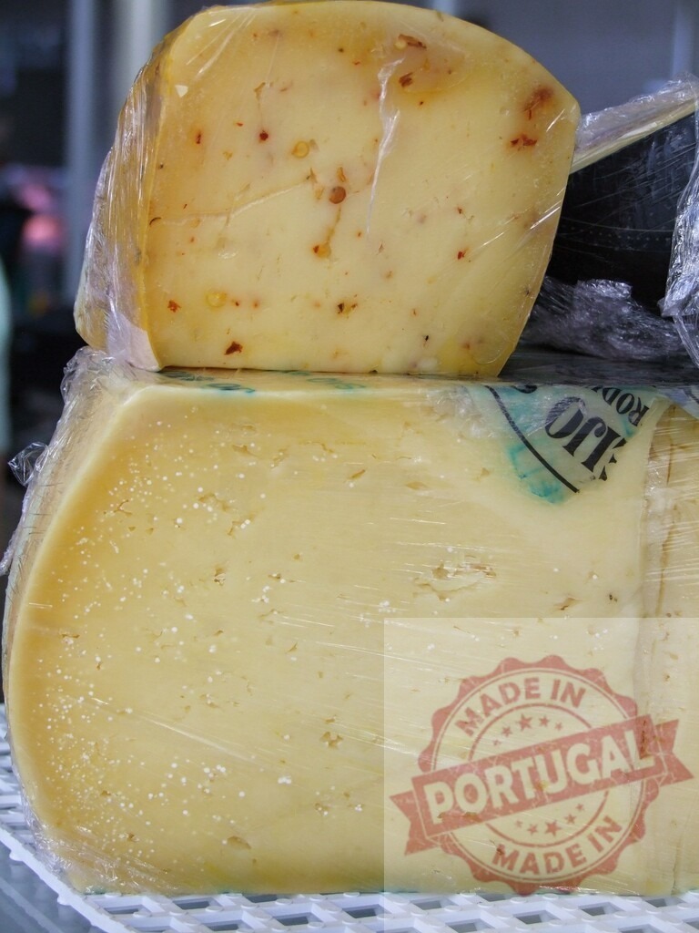 Pepper jack and aged cheese wheels wrapped for market sale | Blocks of pepper jack and aged cheese displaying textures and specks, wrapped in plastic - Realisiert mit Pictrs.com