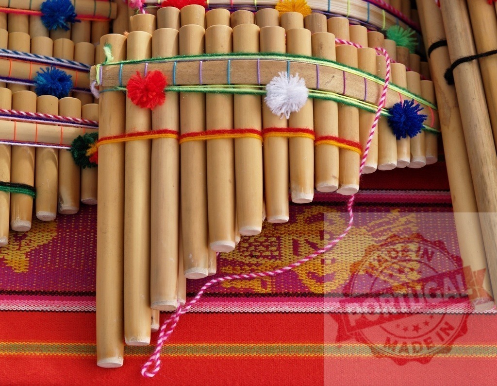 Peruvian panpipes resting on colorful andean textile | Traditional Andean panpipes, also known as zampoñas, handcrafted with bamboo and adorned with colorful yarn pompoms, rest on a vibrant textile - Realisiert mit Pictrs.com