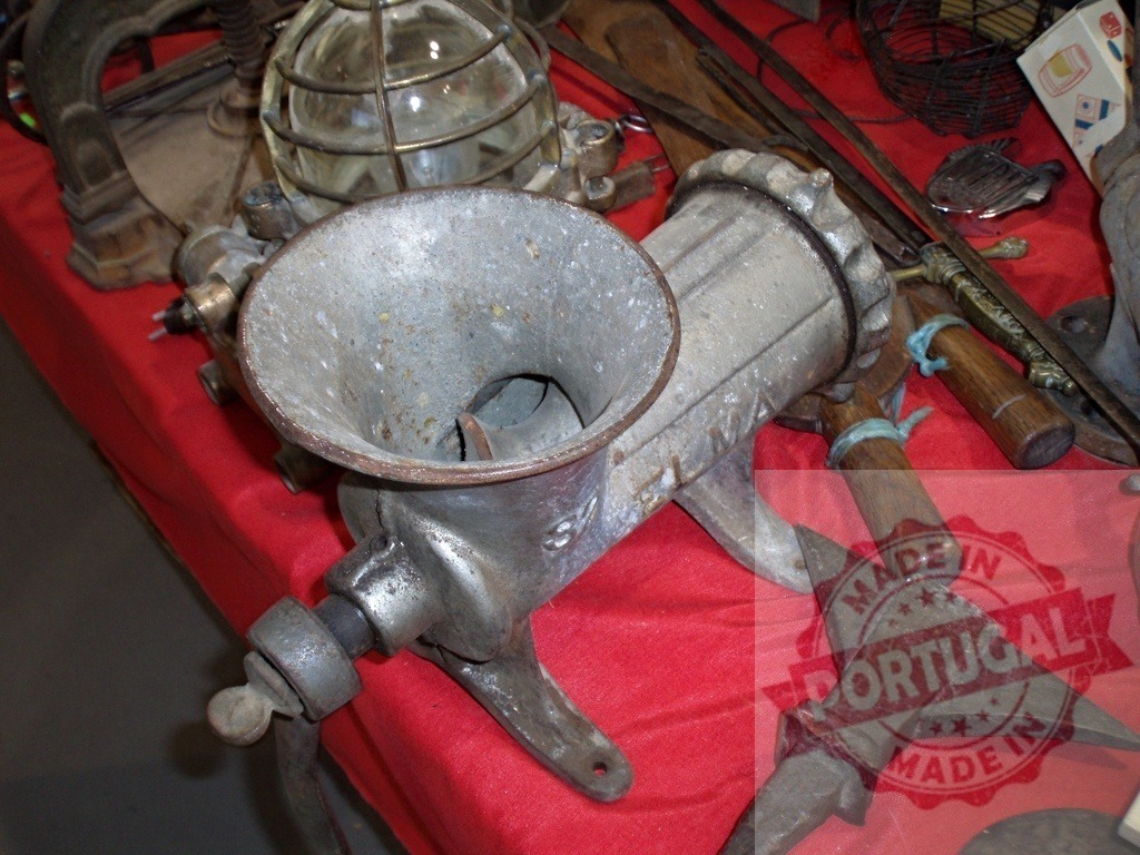 Vintage meat grinder at a flea market stall | Antique metal meat grinder and old tools displayed on a red table - Realisiert mit Pictrs.com