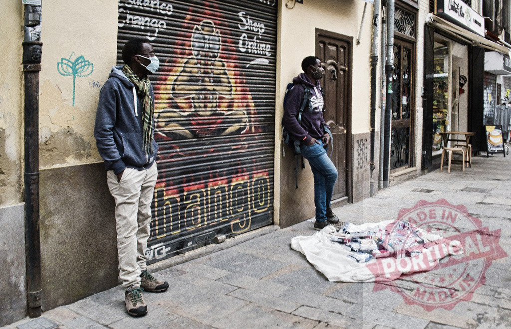 Street vendors wearing face masks selling merchandise | Two young men wearing face masks standing on an urban street selling items on a blanket - Realisiert mit Pictrs.com