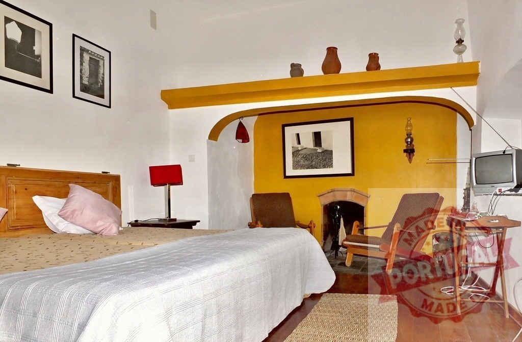 Cozy bedroom with yellow fireplace and traditional decor | Inviting bedroom interior featuring a wooden bed, red lamps, yellow fireplace, and old television - Realized with Pictrs.com
