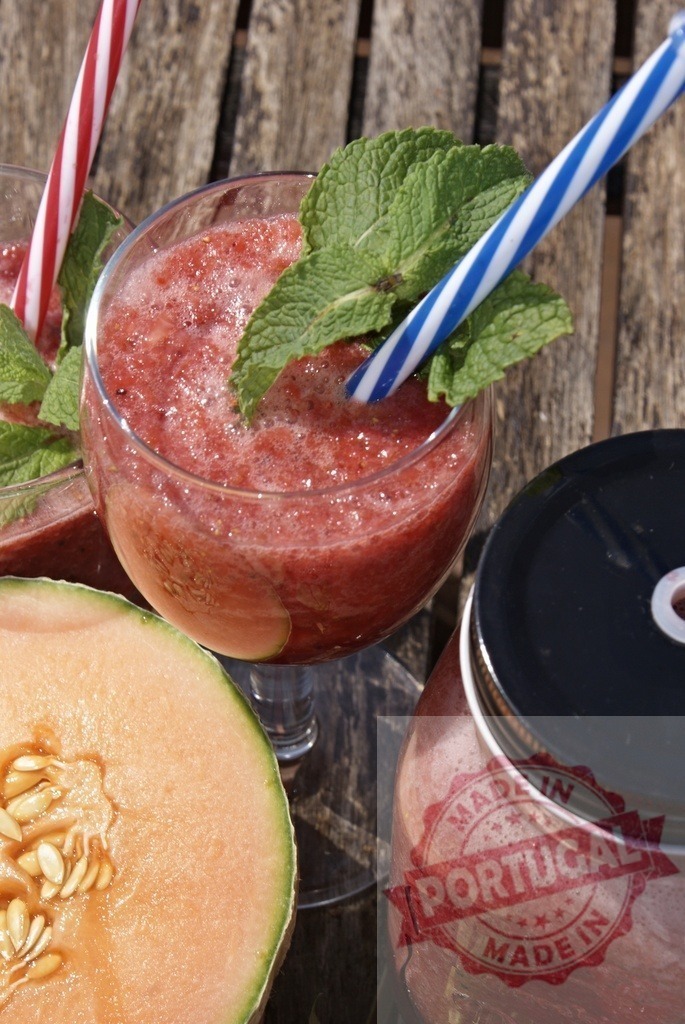 Refreshing strawberry cantaloupe smoothie on wooden table | Red berry smoothie with mint and striped straws, ready to drink outdoors - Realized with Pictrs.com