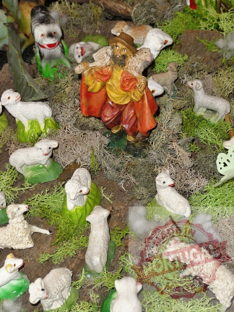Shepherd carrying sheep with his flock and dog in nativity scene | Shepherd figurine carrying sheep with his flock and a dog in a nativity scene, surrounded by moss and greenery - Realized with Pictrs.com