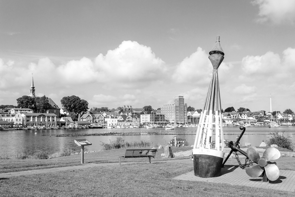 Wandbild: Hafen in Kappeln an der Schlei in Schwarz-Weiß | Erleben Sie die maritime Idylle von Kappeln mit dieser beeindruckenden Schwarz-Weiß-Aufnahme. Die malerische Uferlandschaft mit großen Bojen und einem Anker im Vordergrund fängt die reiche Seefahrtsgeschichte der Region ein. Die friedliche Atmosphäre und die charmante Stadt im Hintergrund machen dieses Wandbild zu einem perfekten Hingucker für Ihr Zuhause.Erhältlich auf Leinwand, Alu-Dibond, Acrylglas, Fineart und als Akustikbild. - Realisiert mit Pictrs.com