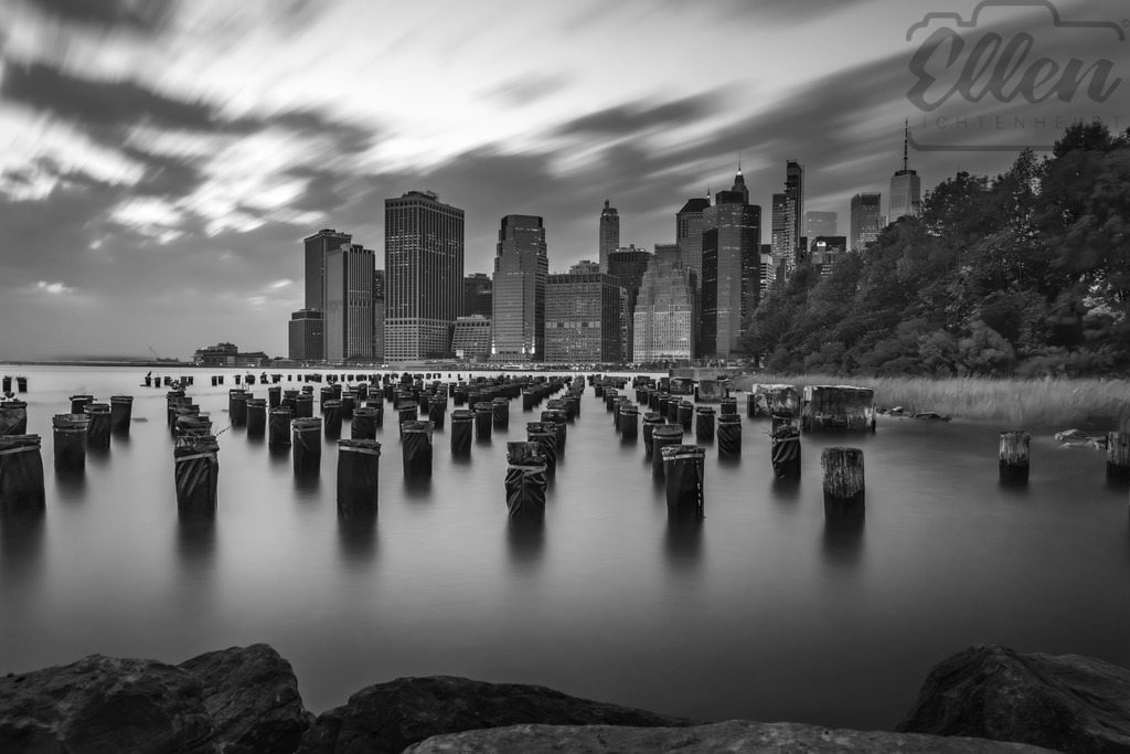 Traces of Time | Old wooden pylons reach out from the East River toward the Manhattan skyline — remnants of the past facing the pulse of modern life. In black and white, New York reveals its quiet side, where time, water, and architecture meet in poetic stillness. - Realisiert mit Pictrs.com