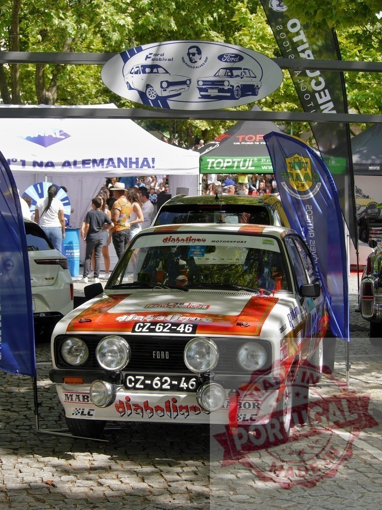 Ford Escort rally car at Ford Festival in Portugal | Vintage Ford Escort rally car displayed at an outdoor car show with trees and people - Realized with Pictrs.com