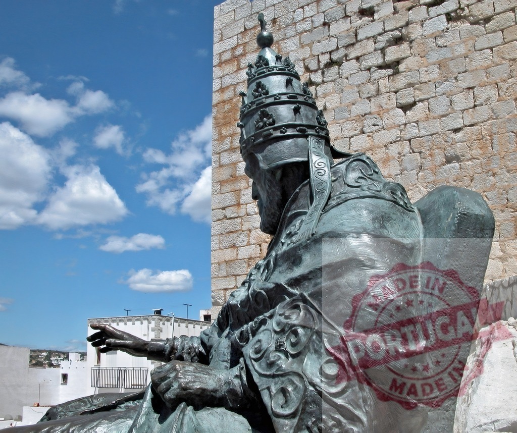 Pope Benedict XIII statue at Peniscola castle. Provincia de Castellon | Bronze statue of Pope Benedict XIII, also known as Papa Luna, with a historic castle wall - Realisiert mit Pictrs.com