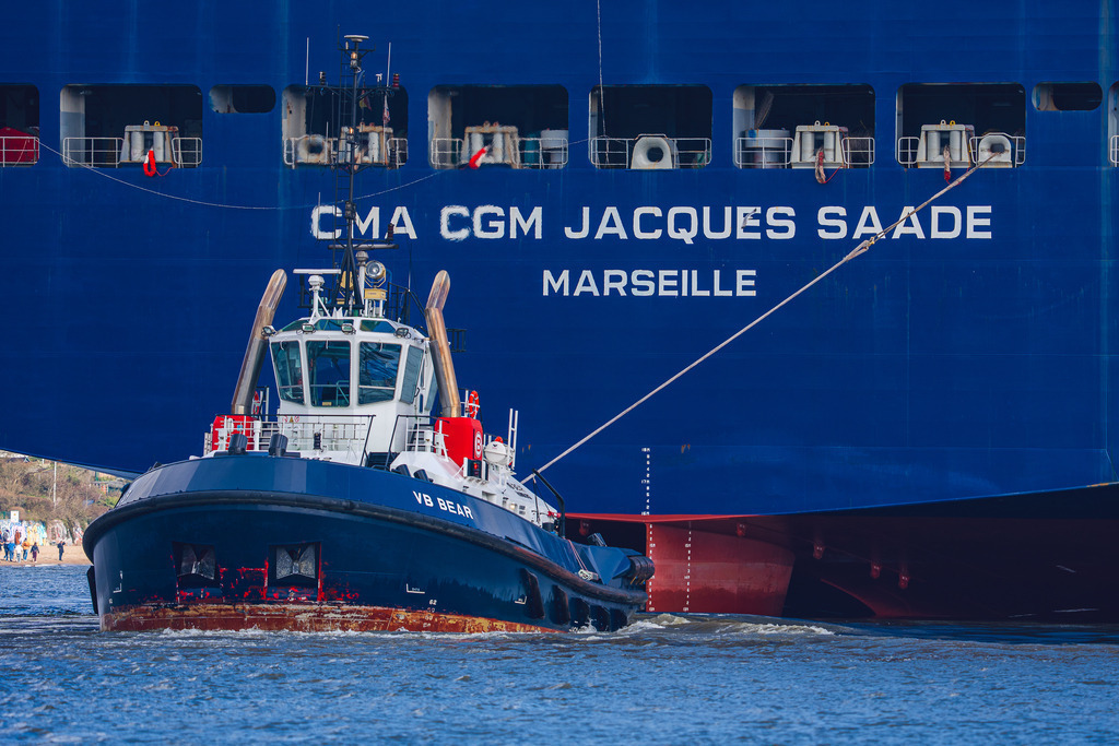 Assistenz am Heck: VB BEAR und Jacques Saadé | Der Assistenzschlepper VB BEAR im Einsatz am Heck des LNG-betriebenen Containerschiffs CMA CGM JACQUES SAADÉ.+´Die Aufnahme zeigt den Moment des Einlaufens in den Hamburger Hafen, in dem der Schlepper über die gespannte Trosse das Manöver des 400 Meter langen Frachters unterstützt. - Realisiert mit Pictrs.com
