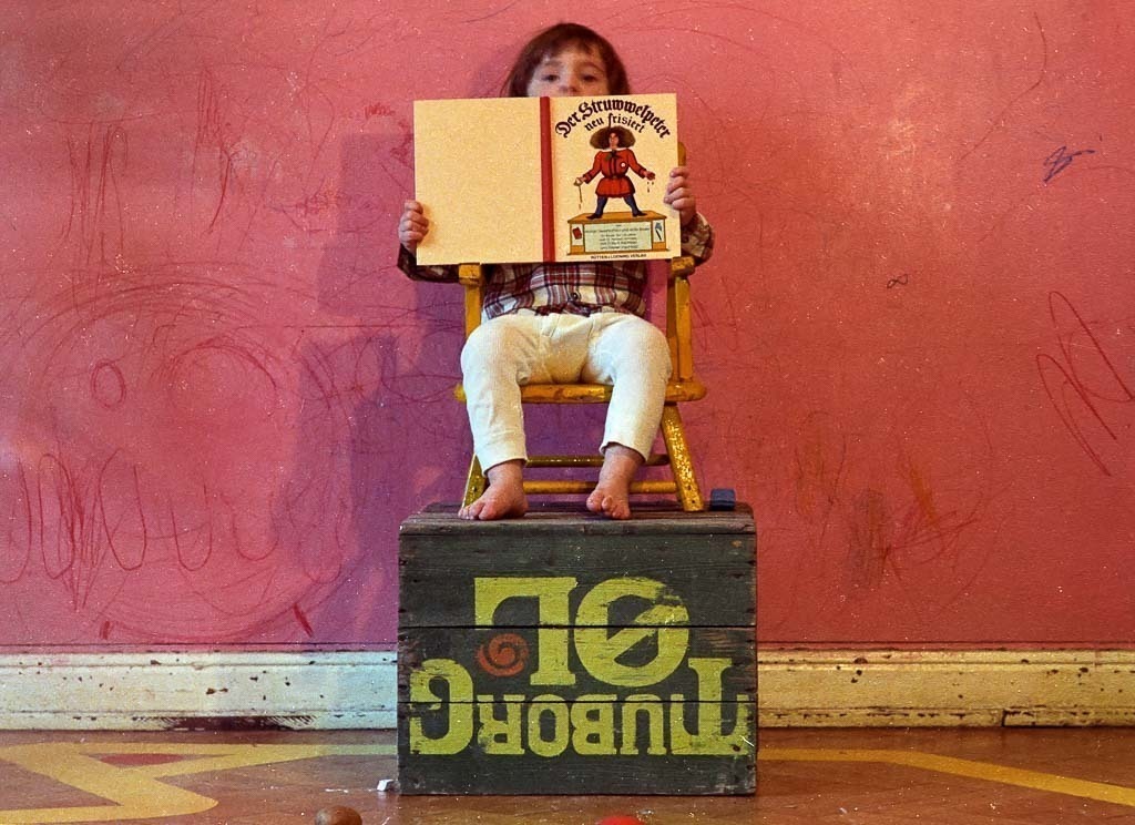 026-1970-142 | Aus der Bildserie über einen antiautoritären Kinderladen in Kiel 1970. Bei dem Buch in der Hand des Jungen handelt es sich um eine 1969 erschienene Parodie auf die klassische Struwwelpeter-Edition von 1844 – passend als Symbol für die unkonventionellen Erziehungsmethoden in dem Kinderladen. - Realisiert mit Pictrs.com