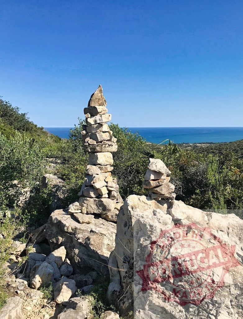 Stacked cairn rocks balancing by the Mediterranean Sea | Stacked rocks form cairns overlooking the tranquil blue sea on a sunny day - Realisiert mit Pictrs.com