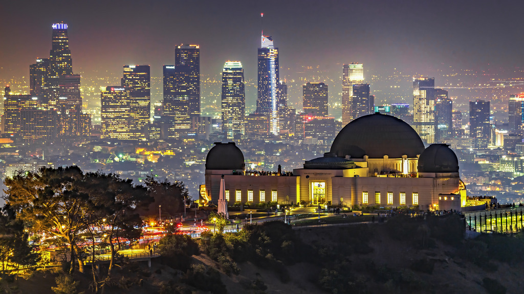 Wandbild - Griffith Observatory und die funkelnde Skyline von Los Angeles | Dieses eindrucksvolle Bild zeigt das Griffith Observatory in Los Angeles bei Nacht, das vor der glitzernden Skyline der Stadt steht. Das Observatorium ist hell erleuchtet und zieht viele Besucher an, die die Aussicht auf die Stadt genießen. Im Hintergrund erhebt sich die eindrucksvolle Skyline von Los Angeles, beleuchtet von unzähligen Lichtern der Wolkenkratzer und Straßen. Der Kontrast zwischen dem historischen Bauwerk und der modernen Stadtlandschaft schafft eine faszinierende und dynamische Szene, die die Energie und das Leben der Stadt bei Nacht einfängt.