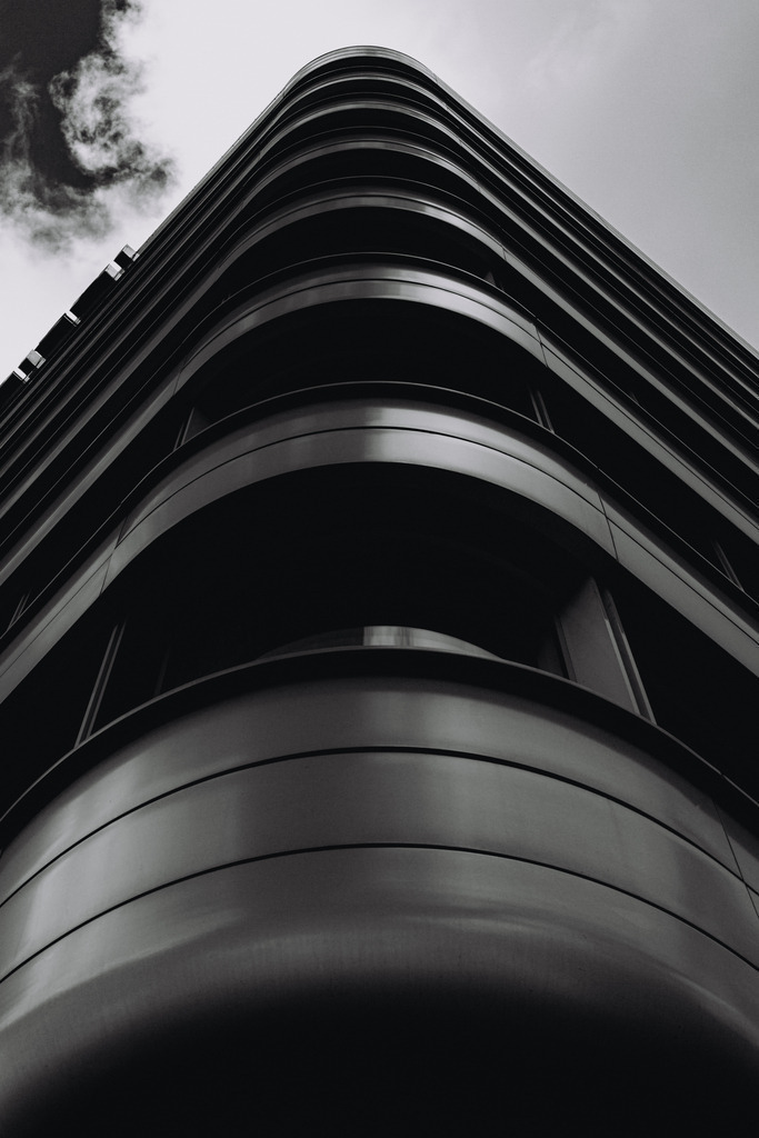 Modern Architecture Curves – Urban Architecture Photography | This fine art photograph shows a modern architectural façade with sweeping curves of steel and glass. The geometric lines guide the viewer's eye upward and create a striking urban composition. Ideal as contemporary architecture wall art for modern living spaces or offices. - Realisiert mit Pictrs.com