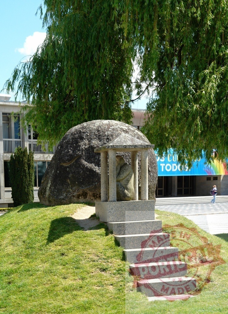 University campus with sculpture and weeping willow tree. Portugal - Norte | University campus featuring a central stone sculpture and large weeping willow tree on a grassy hill - Realized with Pictrs.com