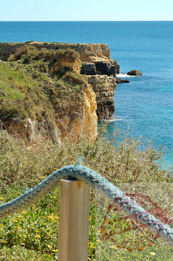 Coastal cliffs and atlantic ocean view in Algarve, Portugal | Rope railing leading to a dramatic seascape with rugged cliffs and blue water - Realized with Pictrs.com