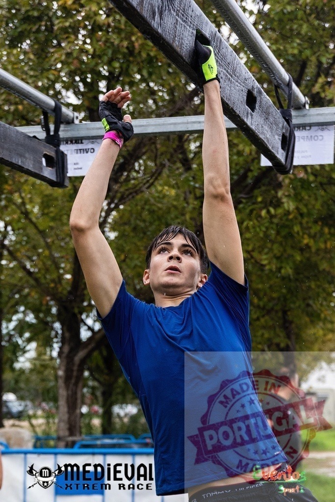 Young man overcoming obstacle course challenge during Medieval Xtrem Race | Athlete hanging on obstacle course, showing strength and determination during an adventure race - Realisiert mit Pictrs.com