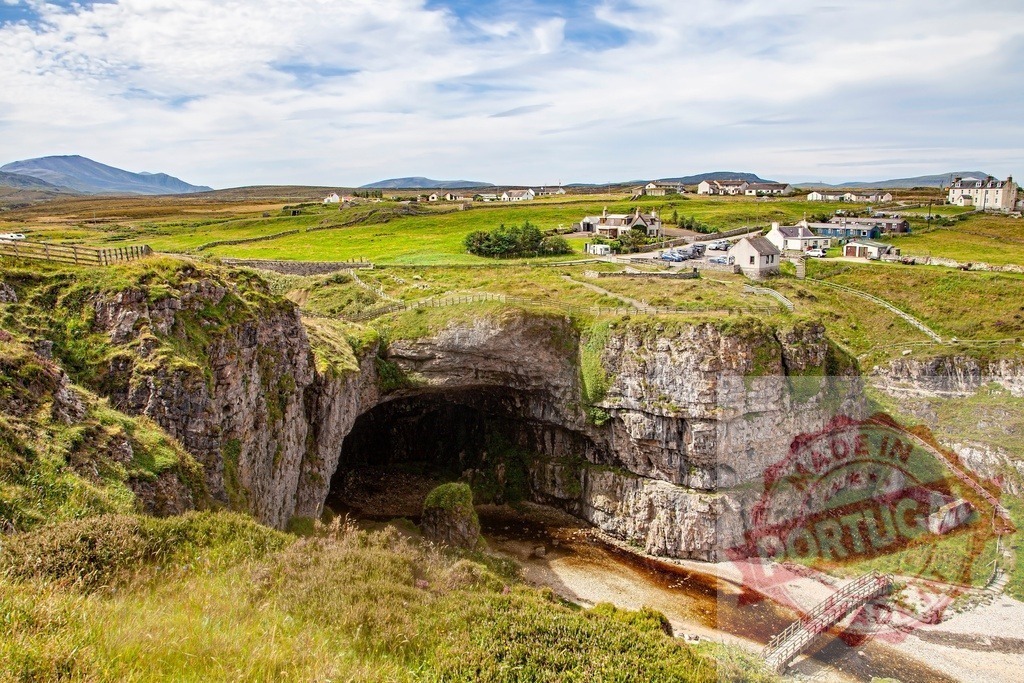 Smoo Cave with scenic landscape views in Durness Scotland | Imposing Smoo Cave, a large sea and freshwater cave, opening to the coastal landscape with village - Realized with Pictrs.com