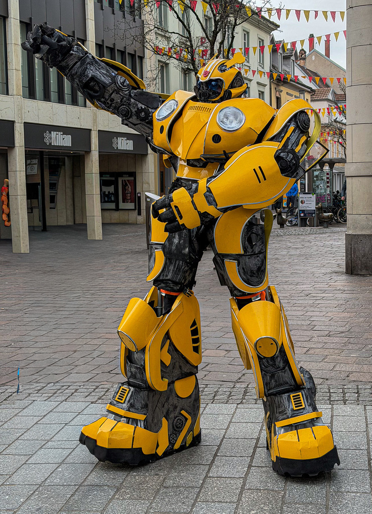 Urban Bumblebee in Lörrach – Street Photography Germany | Unexpected Bumblebee street cosplay spotted in Lörrach city center, Germany.Strong yellow contrast against modern architecture creates a powerful urban character moment.Street photography | Urban portrait | Cosplay in public space | Lörrach Baden-Württemberg - Realisiert mit Pictrs.com