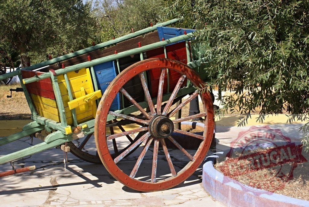 Traditional colorful wooden cart standing in a rustic garden | Rustic wooden cart with vibrant colored panels and large red wheel outdoors - Realized with Pictrs.com