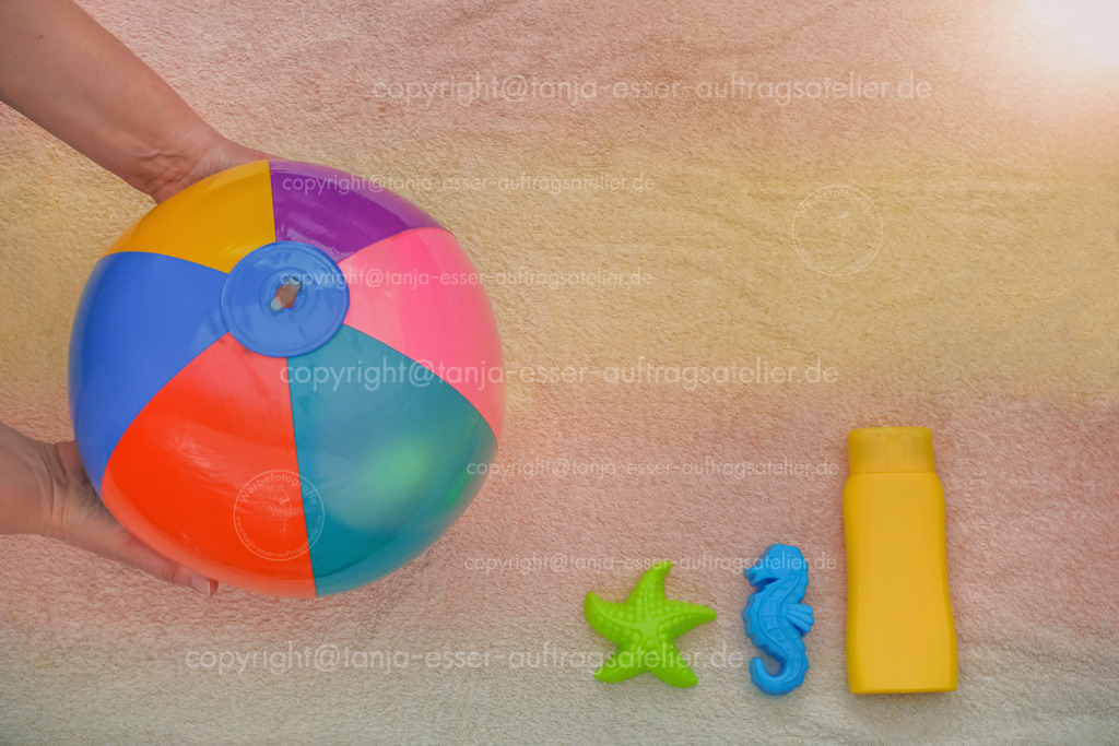 Sunny summer holidays - background | Sonniger Urlaubs Hintergrund. Hände reichen einen aufblasbaren bunten Ball. Rechts befinden sich farbenfrohe Flasche Sonnenmilch als Mock Up und Sandförmchen. Rechts oben ist Copy Space. 