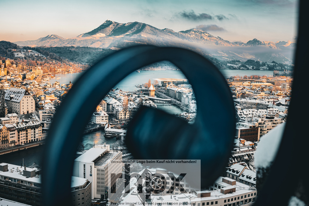 Blick durch das Geländer auf Luzern | Perspektive. Weite. Winter. Ein kunstvoller Rahmen lenkt den Blick auf das verschneite Luzern und die majestätischen Berge im Hintergrund. Das sanfte Licht der tiefstehenden Sonne verleiht der Stadt eine unvergleichliche Ruhe und Eleganz. Wähle unter "Produktauswahl" dein Wunschformat: Vom klassischen Wandbild über Puzzle &amp; Tassen bis zum digitalen Download (z.B. als Handy-Hintergrund). - Realisiert mit Pictrs.com