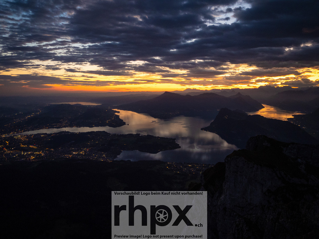 Sonnenaufgang über dem Vierwaldstättersee | Dämmerung. Weite. Licht.Während die Lichter im Tal noch funkeln, bricht am Horizont bereits der neue Tag an und taucht die Wolken in dramatisches Gold. Dieser atemberaubende Blick vom Pilatus auf den Vierwaldstättersee fängt die magische Ruhe zwischen Nacht und Morgen perfekt ein.Wähle unter "Produktauswahl" dein Wunschformat: Vom klassischen Wandbild über Puzzle &amp; Tassen bis zum digitalen Download (z.B. als Handy-Hintergrund). - Realisiert mit Pictrs.com