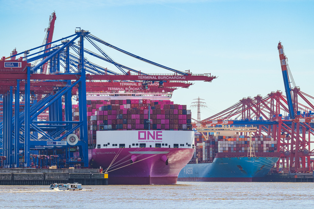 Terminal Burchardkai | Der Burchardkai ist in Hamburg der größte Terminal zur Abfertigung von Containerschiffen. Links im Bild liegt der Containerfrachter ONE INTELLIGENCE, der 400 Meter lang ist; rechts liegt die MOGENS MAERSK, die eine Länge von 399 Meter aufweist. Unten links im Bild fährt eine kleine Barkasse während ihrer Hafenrundfahrt auf den Terminal zu. - Realisiert mit Pictrs.com