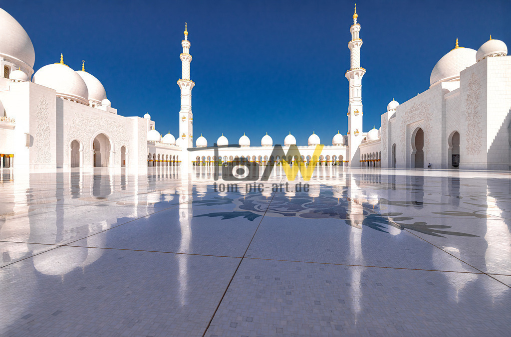 Weitläufiger Innenhof der Scheich Zayid Moschee in Abu Dhabi | Die abgebildete Moschee ist die Scheich-Zayid-Moschee in Abu Dhabi, Vereinigte Arabische Emirate. Sie ist die größte Moschee der VAE und eine der größten der Welt. Die Moschee ist für ihre beeindruckende Architektur bekannt, die aus strahlend weißem Marmor, vergoldetem Messing und Swarovski-Kristallen besteht. Sie verfügt über den weltgrößten handgeknüpften Teppich und einen der größten Kronleuchter der Welt. Die Moschee ist eine der wenigen in der Region, die auch Nicht-Muslimen offensteht und den Dialog zwischen verschiedenen Kulturen fördern soll. Der Bau dauerte 12 Jahre und wurde 2007 fertiggestellt; sie bietet Platz für über 40.000 Gläubige.  - Realisiert mit Pictrs.com