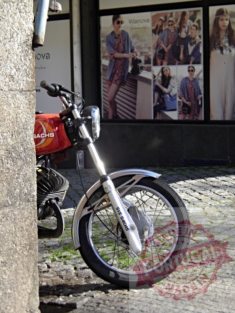 Red vintage Sachs motorcycle parked near fashion store Villanova | Shiny red vintage Sachs motorcycle parked near a fashion store window displaying posters of models wearing Villanova clothing - Realized with Pictrs.com