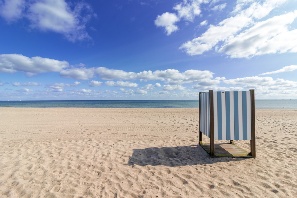 Wandbild: Umkleidekabine am Strand in Weidefeld | Beruhigende Farben und maritime Ruhe – dieses Wandbild bringt die entspannte Atmosphäre des Weidefelder Strandes in den Raum. Die blau-weiß gestreifte Umkleidekabine am Sandstrand verleiht dem Motiv einen freundlichen und harmonischen Akzent, während der offene Himmel mit seinen sommerlichen Wolken eine weitläufige und beruhigende Bildwirkung erzeugt. - Realisiert mit Pictrs.com