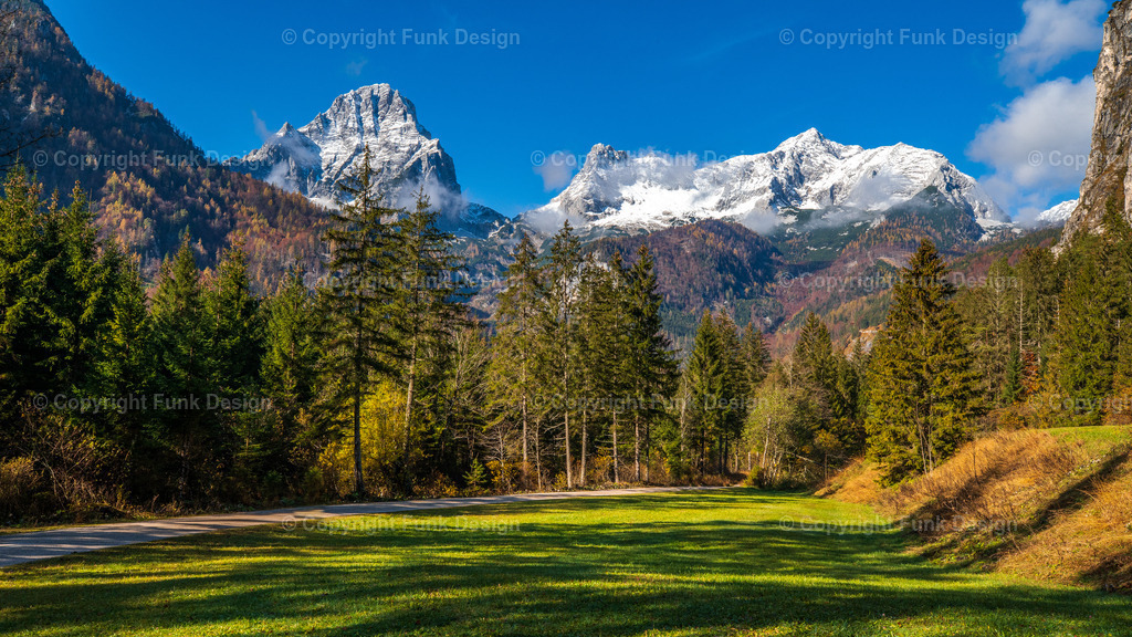 Bergpanorama am Schiederweiher – Hinterstoder, Oberösterreich, Österreich | Der Blick vom Schiederweiher öffnet sich auf ein beeindruckendes Bergpanorama mit frisch verschneiten Gipfeln und tiefgrünem Wald. Die sonnige Wiese im Vordergrund bringt Ruhe und Weite in das Motiv und macht es ideal als Naturbild für Wohn- oder Arbeitsräume.
