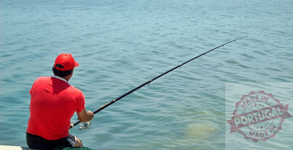 Man fishing with rod in blue ocean water | Man in a red shirt and cap holding a fishing rod over calm blue water - Realized with Pictrs.com